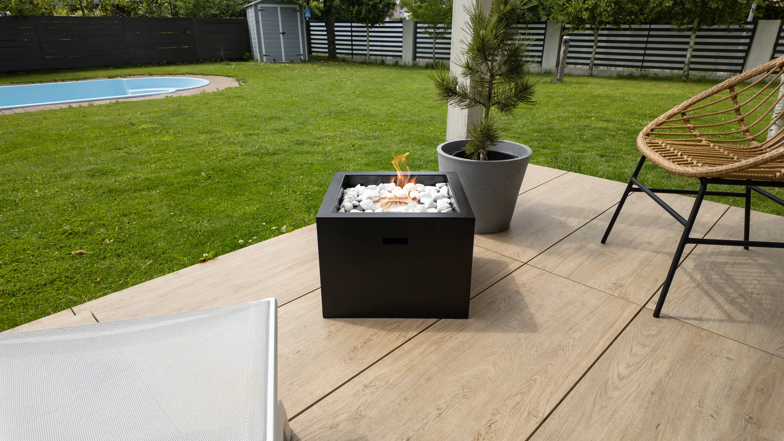 Moderner schwarzer Tischkamin mit weißen Dekosteinen auf Terrasse neben Pflanzen